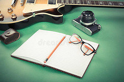 绿色背景上有记事本、铅笔、眼镜和旧相机的电吉他。 过滤后的复古图像