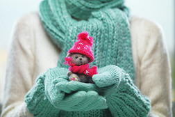 女性手拿着可爱的泰迪熊。 女人双手戴着泰尔手套，展示泰迪熊礼物连衣裙，粉红色针织帽子和围巾。