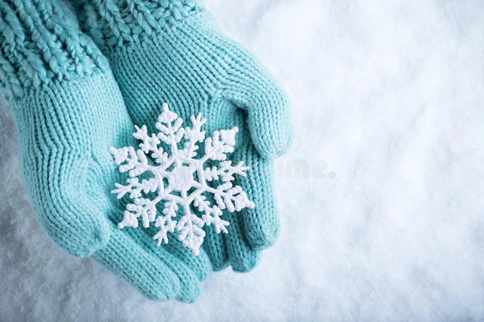 女性的手在白色的雪背景上白色的泰尔针织手套与闪闪发光的美妙雪花 冬天圣诞节的概念