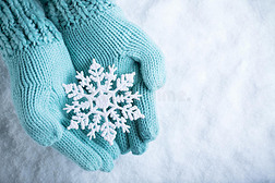 女性的手在白色的雪背景上，白色的泰尔针织手套与闪闪发光的美妙雪花。 冬天，圣诞节的概念