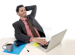 商人靠在椅子上，在办公室电脑笔记本电脑上工作，看上去很高兴、满意和放松