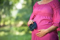 美丽的孕妇带着婴儿鞋站在绿色的草地上