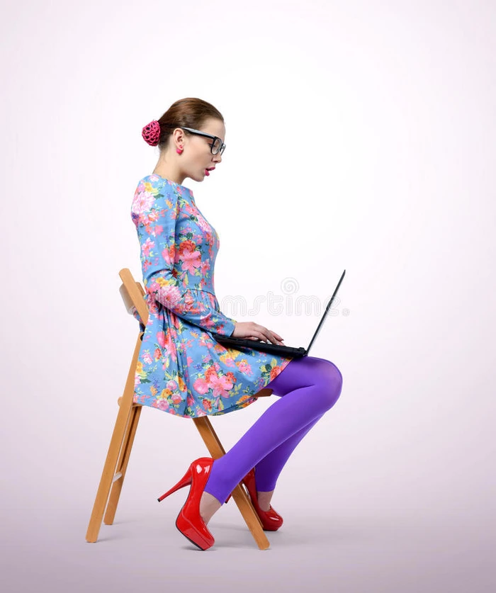 戴眼镜的时髦年轻女人坐在椅子上拿着笔记本电脑