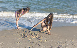 女孩们在夏天的阳光下在沙滩上画画。