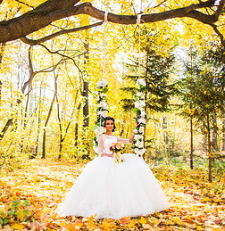 美丽的新娘坐在秋天公园的秋千上