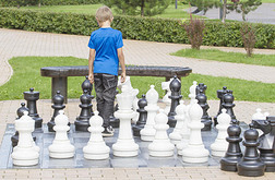 集中注意力的孩子想着他的下一步行动坐在一张木制的长凳上在户外国际象棋游戏中使用生命大小的棋子
