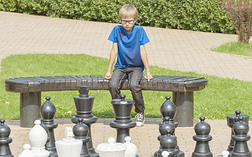 集中注意力的孩子想着他的下一步行动坐在一张木制的长凳上在户外国际象棋游戏中使用生命大小的棋子