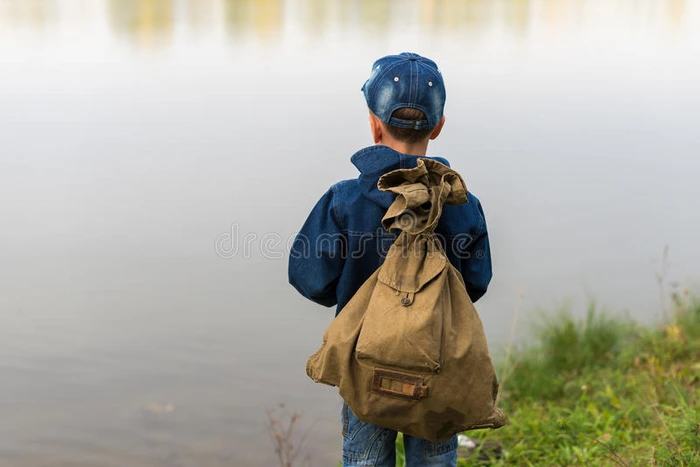一个男孩背着背包站在河岸上