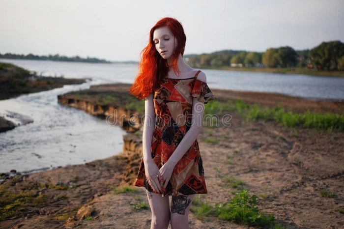 站在河的背景上，穿着太阳裙的漂亮红头发女孩