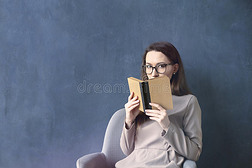 坐在阁楼办公室里读古董书的漂亮女商人。 看看打开的书棕色封面。 深蓝色的墙壁背景