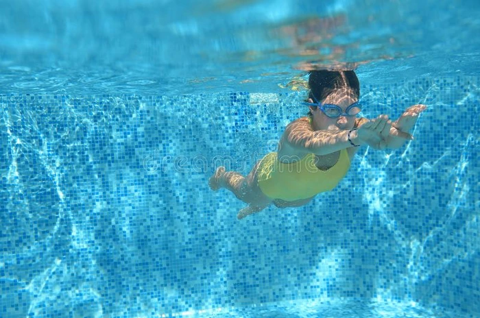 年幼的女孩游泳者游泳在下面水采用水池和有乐趣,球座