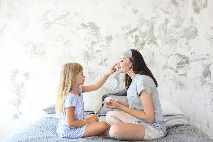 漂亮的微笑的母亲和女儿应用面容乳霜