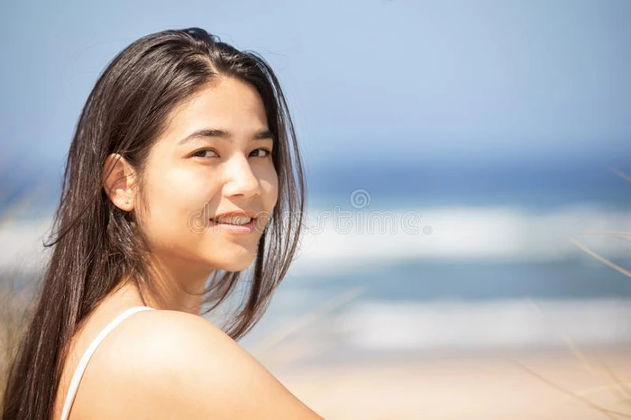 美丽的青少年女孩在海滩向和煦的照到阳光的一天,微笑的